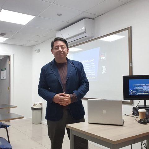 Paulo Rebolledo dando una clase, de pie junto a un notebook y frente al proyector